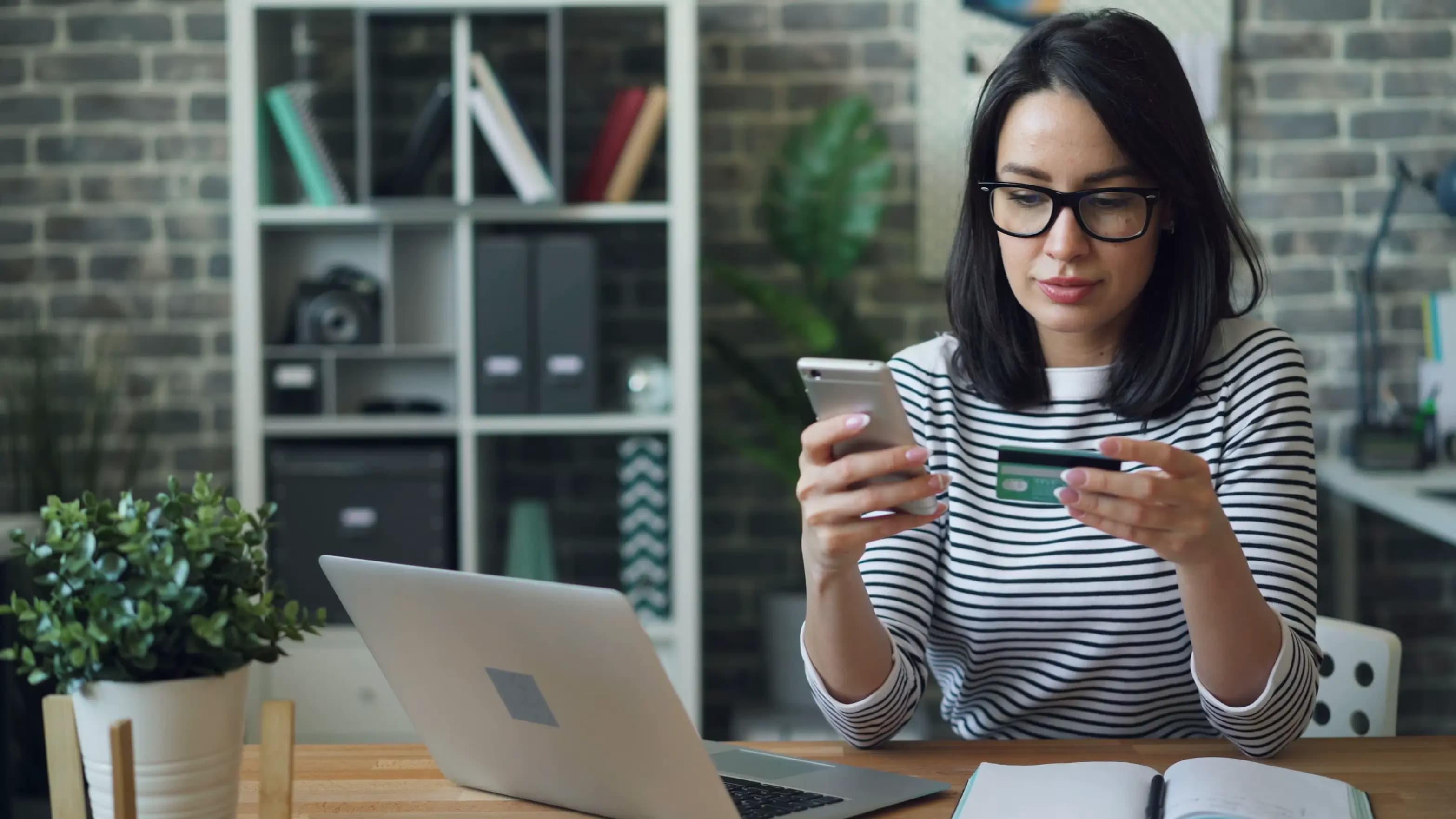A woman using her phone and holding a payment card